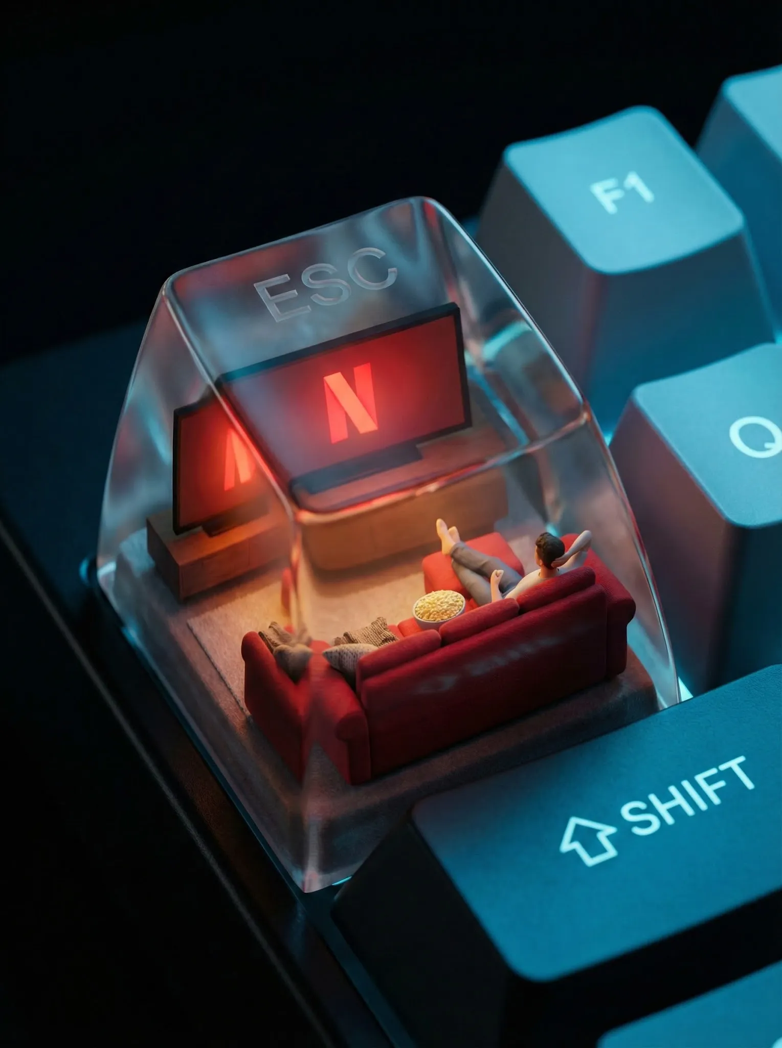 A photorealistic ESC keycap scene shows a miniature cozy living room setup. Inside: a glowing red Netflix screen, a plush red couch, popcorn bowl, and throw blanket. A small figure lounges with feet up, watching content. The red “N” logo glows from behind like mood lighting. Outside: cool tech-blue reflections on F1, Shift, and Q keys. The word “ESC” is subtly present in a glassy fog on top of the cap.